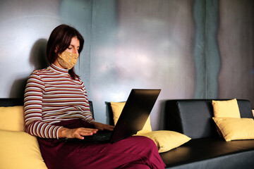 a woman using protective mask and working with a laptop - new normal