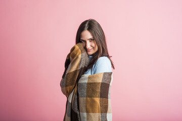 Portrait of a brunette girl who is wrapped in a blanket in the studio on a pink background