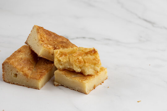 Pieces of freshly baked white chocolate brownies in square form. Flat lay composition with sweet white brownies isolated on white marble background. Delicious blondie brownies. Dessert menu concept.