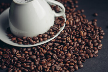 inverted white cup on a platter and sprinkled coffee beans on a dark background