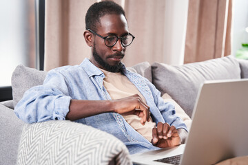 Man attentively looking at the laptop screen while sitting at the living room