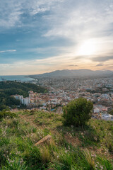 Fototapeta na wymiar Beautiful sunset views of the city of Malaga from a viewpoint on a hill with grass and plants, overlooking the city, the sea, the mountains and the cloudy sky in the background.