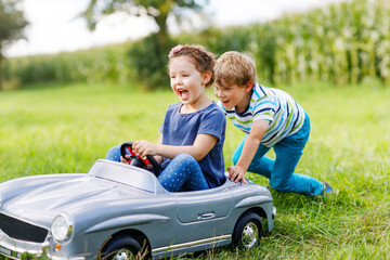 Two happy children playing with big old toy car in summer garden, outdoors. Boy driving car with...
