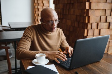 Focused african man wearing headphones watching webinar training making notes study online learning language on computer, black male student looking at laptop elearning in internet write information