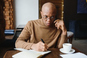 African-Ameican entrepreneur wearing shirt with rolled up sleeves looking through window with thoughtful and serious face expression, feeling nervous before meeting with business partners at cafe