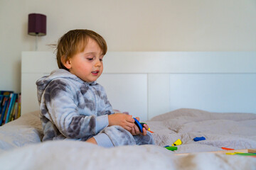 Little toddler boy plays on the bed in a wooden magnetic constructor, preschool child learning at home to make mosaic. Early development. Playing with chikldren during coronavirus outbreak.