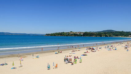 Fototapeta na wymiar Panoramic view of the sandy beach of Miño in the Galicia region of Spain, with beach goers enjoying the summer weather.