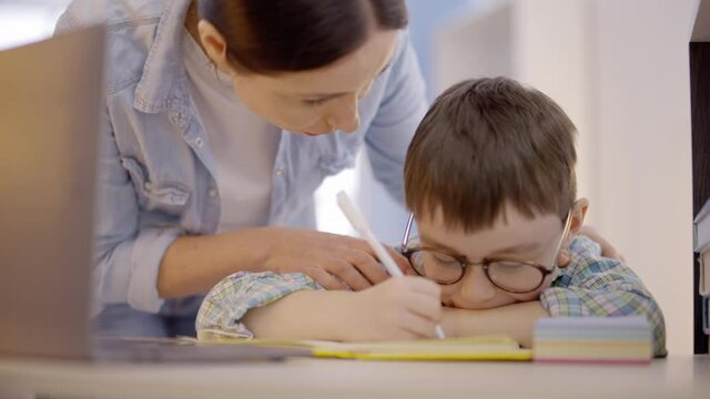 Young mother arguing with child, doing homework at table, learning difficulties