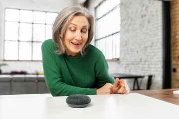 Senior elderly modern woman is using voice commands for wireless smart speaker control. Smart home and technology concept