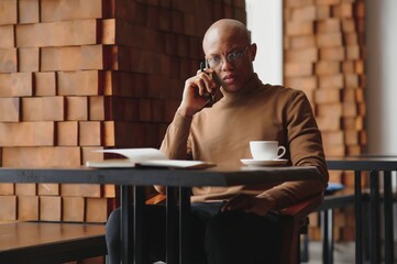 Concentrated black male entrepreneur reads paper documents sitting in cafe with coffee near window.