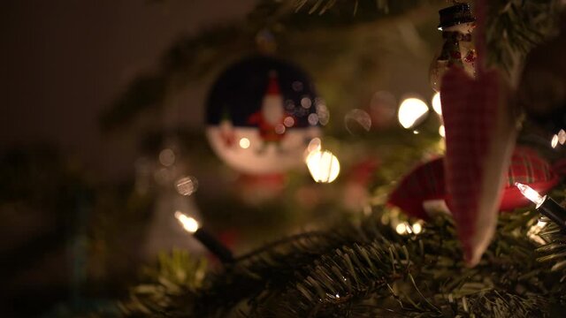 Slow pull focus from a love heart ornament in a real fir christmas tree to an Elf bauble