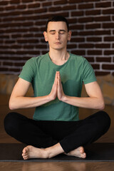 Handsome young man meditating in the living room