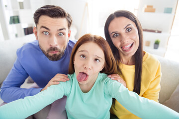Photo of cheerful family mommy daddy daughter happy positive smile have fun grimace fooling tongue-out make selfie home - obrazy, fototapety, plakaty