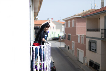 Obraz na płótnie Canvas Una mujer joven que sujeta un libro con una mano y saluda con la otra desde el balcón 