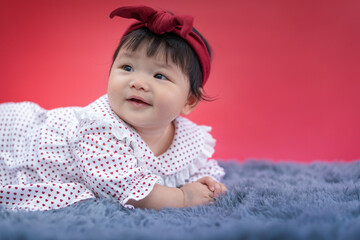 Asian happy baby crawling and smiling on carpet with red color background. Cute 6 months baby start crawling with copy space use as concept of valentine, love, baby or kid department in hospital.