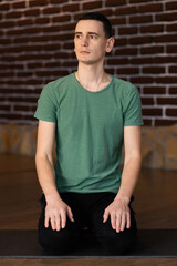 An adult man meditating at home, sitting on yoga mat