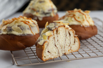 Close-up of delicious cinnabons on a cooling tray on white marble background. One is cut in half. Cinnamon rolled buns with white sticky glaze, almond flakes and caramel on top. Dessert buns pastry.