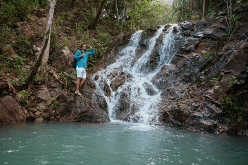 Male tourist near a small mountain tropical lake and waterfall.