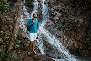 Male tourist near a small mountain tropical lake and waterfall.