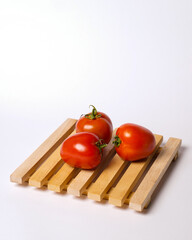 Three tomatoes on a wooden square isolated on white background. Apart from being used as a cooking ingredient, tomatoes can be used as juice. Consuming tomatoes can also help burn fat. Mockup tomato. 