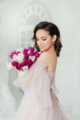 An attractive young woman holds a bouquet of white and purple tulips in her hands. Beautiful girl in a lush dress