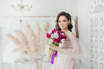 An attractive young woman holds a bouquet of white and purple tulips in her hands. Beautiful girl in a lush dress