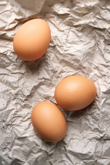 Chicken eggs. Top view of three raw brown chicken eggs on crumpled wrapping paper. High calorie protein food concept.