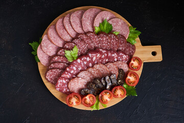 Assorted sliced sausages of different flavors. Served on a beautiful wooden tray, with herbs and cherry tomatoes