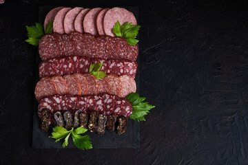 Assorted sliced sausages of different flavors. Served on a black board tray, with herbs and cherry...