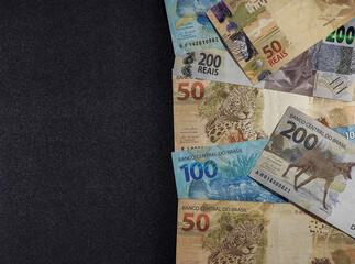 various money notes of 50 reais 100 reais and 200 reais from brazil on a black background. space for text. money from brazil. earn money. Real, Currency, Money, Dinheiro, Reais, Brasil.