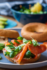 Bagel sandwiches in the making. Gluten free toasted bagel with smoked salmon, cream cheese and lettuce. Avocado, tomatoes and cucumber in background. Homemade Healthy breakfast with fun vibrant colors