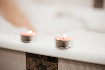 Two pink scented candles. Atmosphere of relaxation and tranquility, pleasure. Girl in foam takes a bath on the background. 