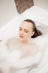 Beautiful portrait of girl with closed eyes takes a bath in white foam. Spa relaxation and self care