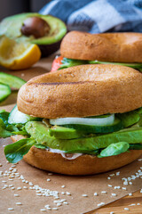 Homemade bagel sandwiches. Gluten free toasted bagel with garlic mayo, avocado lettuce, cucumber and onions. Smoked salmon bagel in background on a baking sheet. Healthy breakfast, fun vibrant colors