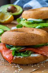 Homemade bagel sandwiches. Gluten free toasted bagel with smoked salmon, cream cheese, cucumber and lettuce. Avocado bagel in the background on a baking sheet. Healthy breakfast, fun vibrant colors
