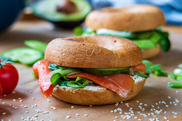 Homemade bagel sandwiches. Gluten free toasted bagel with smoked salmon, cream cheese, cucumber and lettuce. Avocado bagel in the background on a baking sheet. Healthy breakfast, fun vibrant colors