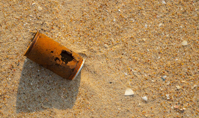 Old rusty can dropped on the sand beach, top view photo.