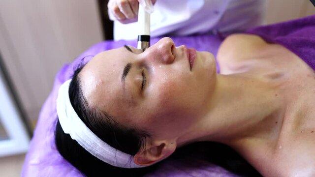 Microcurrent facial massage. Beautician in white gloves holding the electrode of the massage apparatus and syringe. Hardware cosmetology.