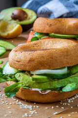 Homemade bagel sandwiches. Gluten free toasted bagel with garlic mayo, avocado lettuce, cucumber and onions. Smoked salmon bagel in background on a baking sheet. Healthy breakfast, fun vibrant colors