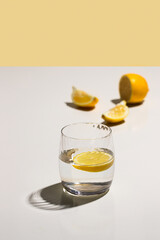 Glass of water with lemon  on beige background with hard light and shadow