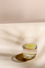 Glass of water with lemon  on beige background with hard light and shadow