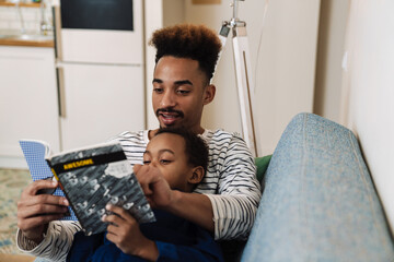 Focused african american father and son reading book on couch