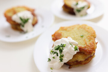 Potato pancakes with sour cream lying on white plate closeup