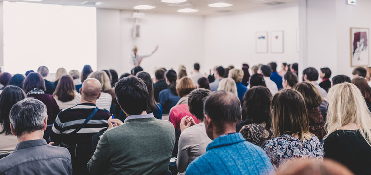 Life Coaching Symposium. Female Speaker Giving Interactive Motivational Speech At Entrepreneurship Workshop. Audience In Conference Hall. Rear View Of Unrecognized Participant.