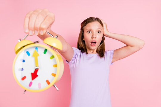 Photo of amazed shocked little girl hold hand head alarm clock oversleep isolated on pink color background
