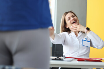 Woman doctor laughing at male patient in shorts in clinic
