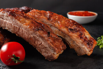 Grilled pork ribs, served on a graphite board with tomatoes