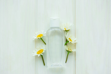 Fresh chamomile flowers with gel bottle on white wooden background. Top view. Copy space