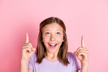 Photo of happy charming little girl point fingers look up empty space solution isolated on pastel pink color background
