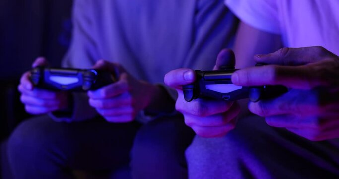 friends playing console video games together. controller in hands closeup. neon lights